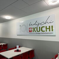 Speisesaal mit großen Logo-Tafeln „badischi Kuchi“